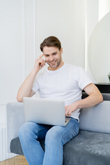 cheerful man using laptop while sitting on sofa at home.
