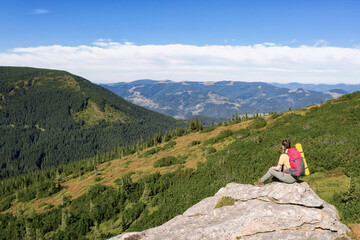 Woman with backpack and sleeping mat on rocky cliff in mountains, back view