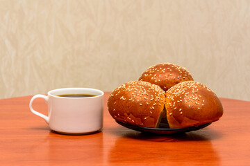 Cup of coffee and buns. Breakfast. Buns sprinkled with sesame seeds. Three buns on a plate. White coffee cup. Morning coffee. Small cup.