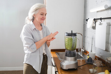 Healthy nutrition in the family, vegetarianism. Senior lifestyle. elderly woman makes smoothie from greenery and superfoods in the kitchen at home