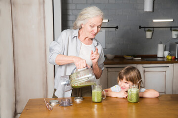 Healthy nutrition in the family, vegetarianism. Senior lifestyle. grandmother and granddaughter drink smoothie from greenery and superfoods in the kitchen at home