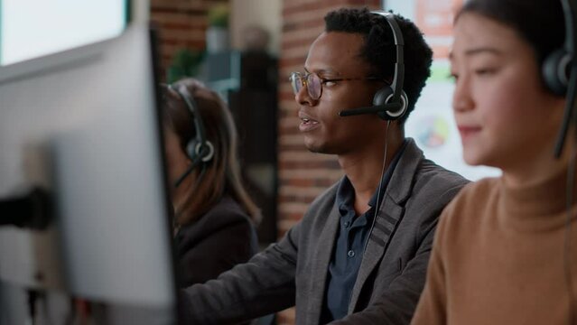 Male call center operator using headset to help people, giving telemarketing assistance to clients on helpline. Person working at customer support service office, offering advice.
