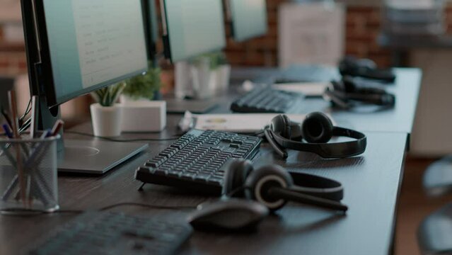 Empty call center office with computers and audio headsets used to have conversation with people on customer service helpline. Nobody at telemarketing workstation with technology.