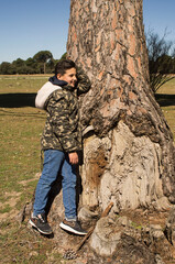 Boy posing next to a tree trunk wearing a camouflage jacket.