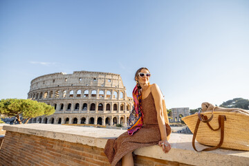 Portrait of a cheerful woman on background of Coliseum in Rome on a summer time. Concept of visiting famous landmarks and travel Italy. Girl wearing dress and colorful shawl - obrazy, fototapety, plakaty