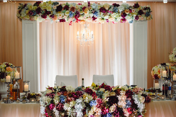 Festive table, arch, stands decorated with composition of pink, white, purple flowers and greenery, candles in the banquet hall. Table newlyweds in the banquet area on wedding party.