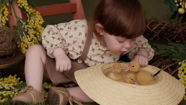 Cute red-haired little girl in vintage dress playing with duckling in straw hat.Easter decorations.Spring and Easter concept.