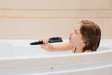 cheerful girl washes, plays and sings into comb like microphone in bathroom