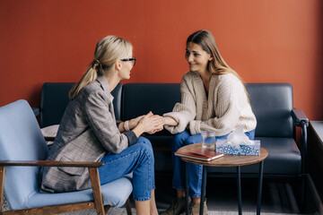 Empathic female psychologist holding female client's hand giving mental professional support - obrazy, fototapety, plakaty
