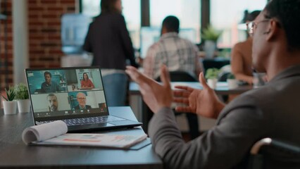 African american man talking to colleagues on videocall meeting, using laptop in business office. Male employee with disability attending online videoconference for remote telecommunication. - Powered by Adobe