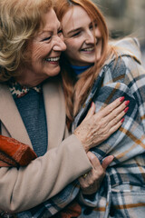 Grandmother and adolescent granddaughter are hugging during the walk on the street in cold weather.
