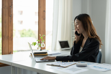 Obraz premium Asian Businesswoman Talking On Mobile Phone Working On Laptop for financial In Modern Office.