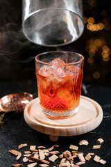 Cocktail served on a wooden board with a glass dome and smoke close-up.