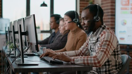 African american man working at call center office to help people with telemarketing assistance. Male employee using headphones and microphone at customer care service. Tripod shot.