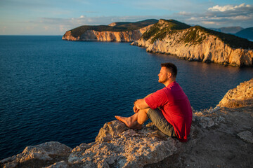 man enjoying sunset above the sea sitting on the cliff