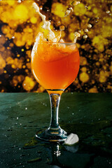 Multifruit juice in a glass with splashes and splashes with pieces of ice and flying drops, a juicy drink in a beautiful color on a bright background