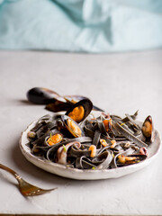 black noodles with seafood in a white plate on a light background. Black pasta of Asian Cuisine