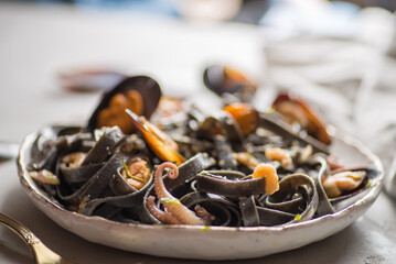 black noodles with seafood in a white plate on a light background. Black pasta of Asian Cuisine