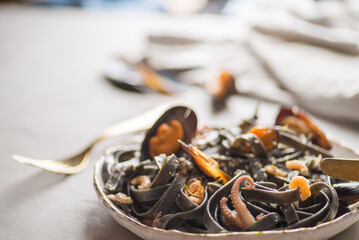 black noodles with seafood in a white plate on a light background. Black pasta of Asian Cuisine