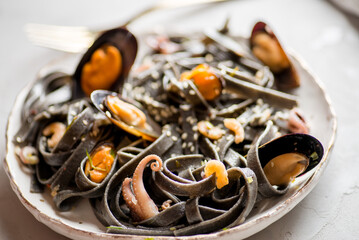 Fototapeta premium black noodles with seafood in a white plate on a light background. Black pasta of Asian Cuisine