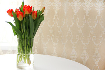 a bouquet of red tulips in a glass vase on a white table. Spring bouquet of flowers in a vase