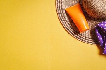 Orange sunscreen tube, straw hat on a yellow background. Summer beach travel essentials, sun protection cream with spf. Top view, flat lay photography