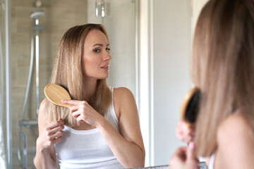 Young caucasian woman brushing hair in the bathroom