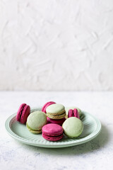 Pink and green macaroons on green plate on white background. Traditional French sweet dessert.