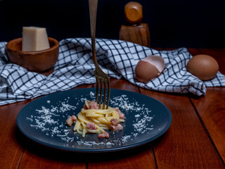 A plate of carbonara-style rolled spaghetti, with a fork skewered on top