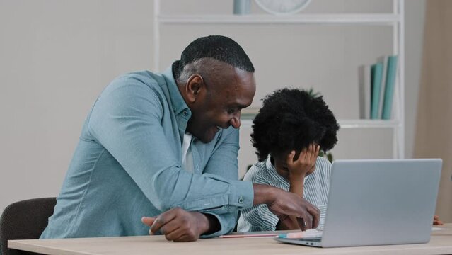 Adult father home teacher helping little daughter to do homework sit at desk in room study remote using laptop man explaining kid girl task african american family having fun together laughing smiling