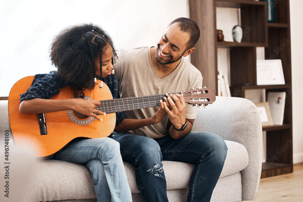 Sticker Dad, every daughters number one fan. Shot of a young girl learning to play the guitar with her father at home.