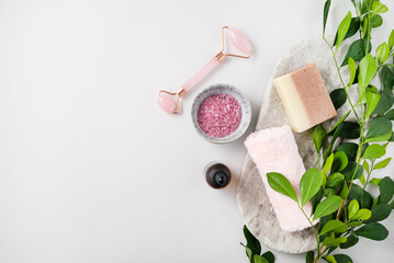Concept flat lay of facial and body care cosmetics with pink sea salt, soap, massager, towel and cream on white  background with brunch. Top view and copy space