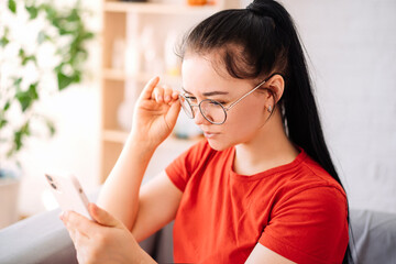 A girl with glasses with vision problems is trying to read a text on the phone at home. the girl has myopia.