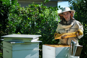 Young female beekeeper hold wooden frame with honeycomb. Collect honey. Beekeeper on apiary. Beekeeping concept.
