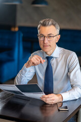 Mid aged man in elegant clothes sitting at the table in a cafe