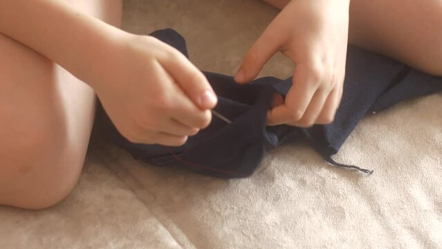Close-up of a boy's hand sewing up his trousers at home. The child learns to sew his own torn clothes. selective focus. Torn children's clothing repair