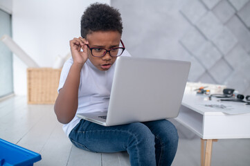 A cute teen sitting at the laptop and looking involved