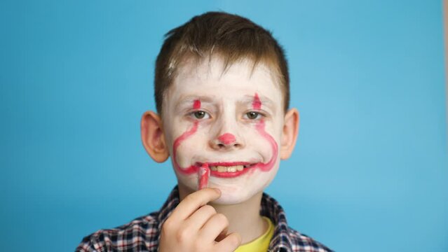 A cheerful caucasian boy puts on his face a scary evil monster make-up, preparing for a masquerade celebration of Halloween. The child is dressing up as a zombie. Kids love Halloween