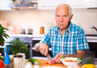 senor man preparing fresh vegetable salad at home in the kitchen