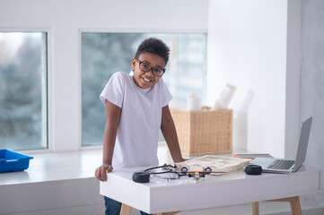Obraz premium A boy in a white tshirt standing at the table with cables and laptop