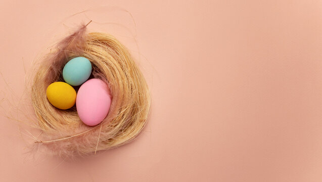 Happy Easter card. colored yellow, pink, blue easter eggs on a beige nest background from above, image with selective focus. Place for text