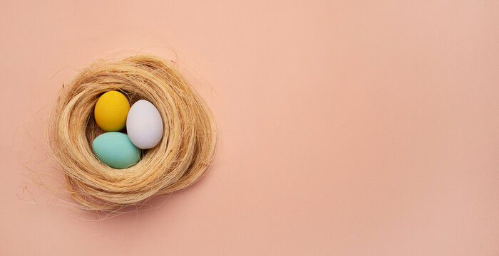 Happy Easter card. colored pink easter eggs on a beige nest background from above, image with selective focus. Place for text
