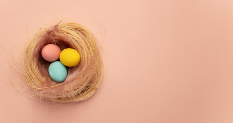 Happy Easter card. colored yellow, pink, blue easter eggs on a beige nest background from above, image with selective focus. Place for text