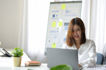 Attractive Asian businesswoman working on laptop in her workstation. Smiling young Asian businesswoman working on a laptop at her desk in office meeting room.