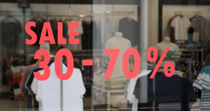 Glass of shop window showcase with discount sticker. Boutique in the mall with clothes on big sale. Offline shopping, display of goods, t-shirts on hangers.