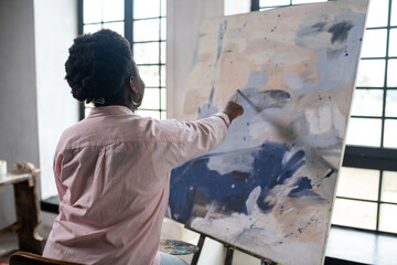 A dark-skinned woman sitting near the easel and painting