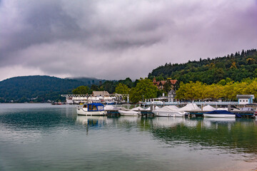 Fototapeta na wymiar Austrian mountain pier with boats on a calm mirroring water in a cloudy autumn morning