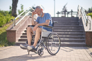 Obraz premium A disabled man in a wheel chair outdoors looking thoughtful
