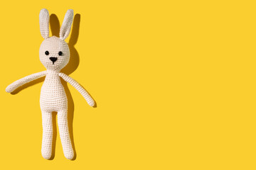 White amigurumi hare lies on a yellow background. Needlework concept. There is a place for text. Cope space. Happy easter. Wide banner