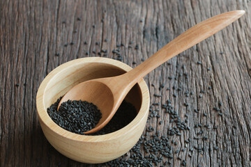 black sesame seeds in a spoon and bowl on a wooden surface background. Shot in natural light.